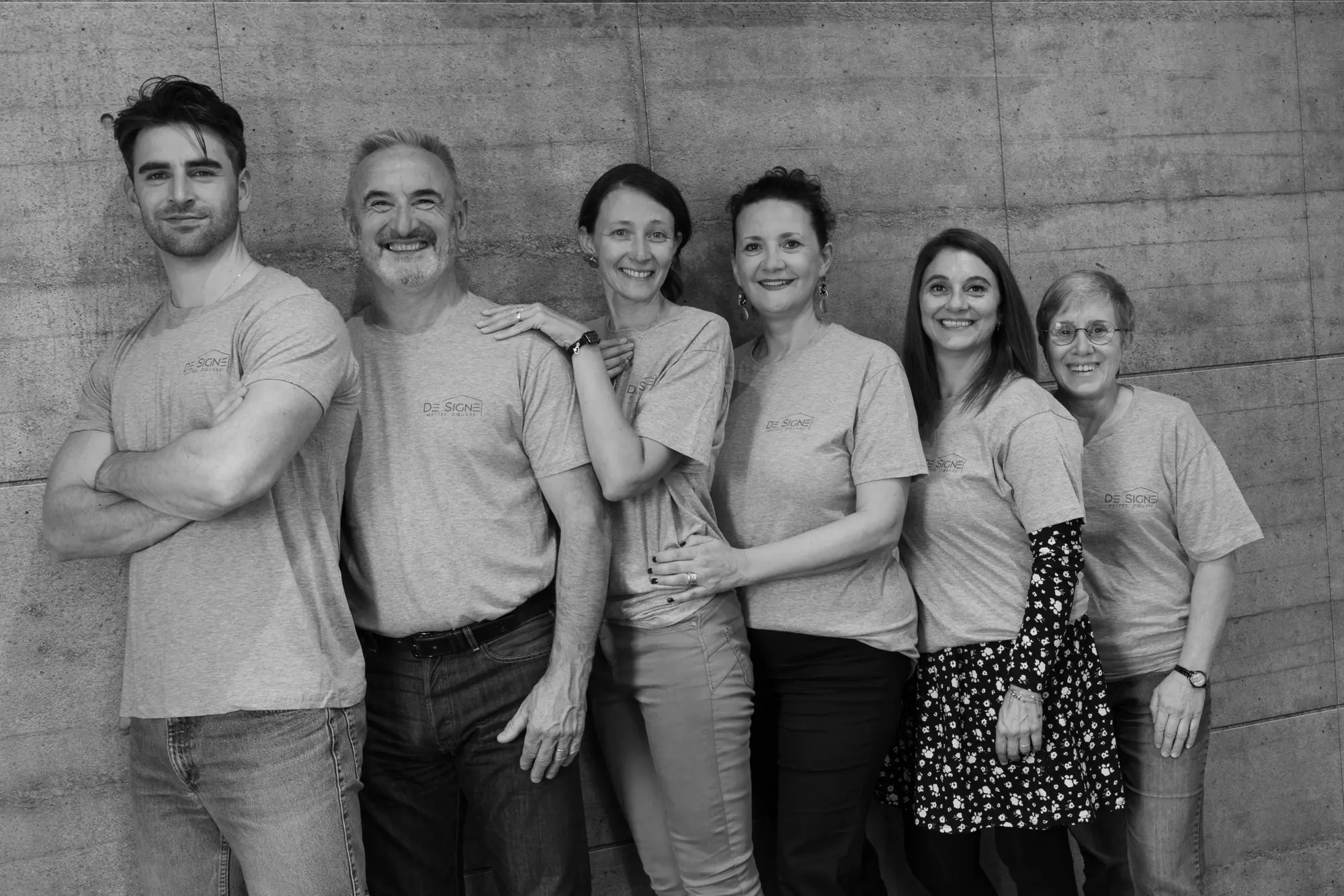 L'équipe de DE SIGNE Concept réunie devant un mur en béton, en tee-shirts DE SIGNE