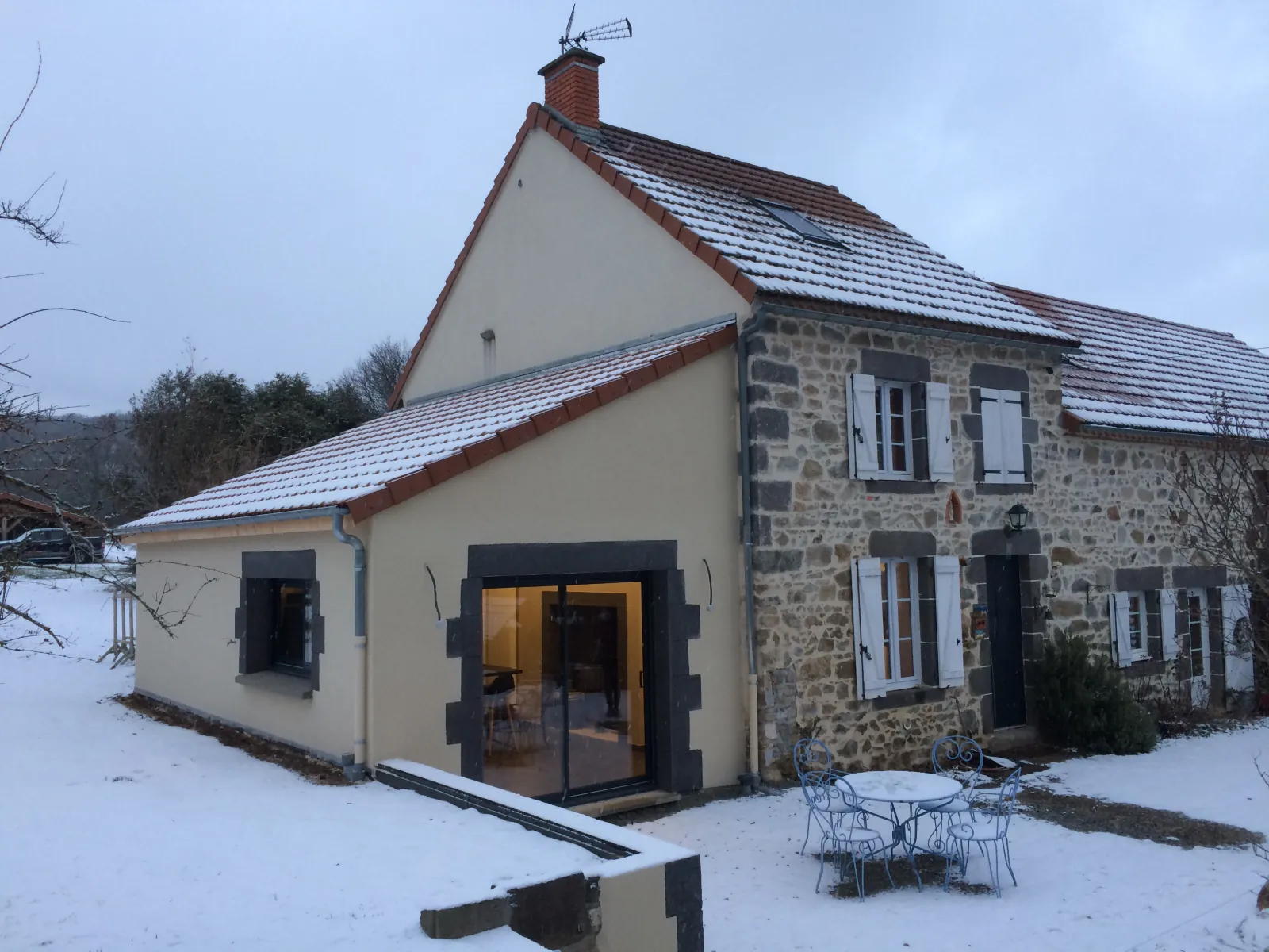 Extension enduite accolée à une maison ancienne en pierre, baie vitrée encadrée de pierre sombre