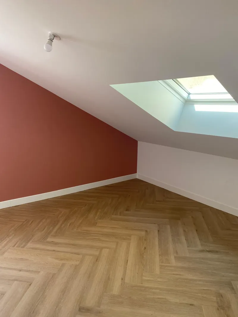 Combles aménagés, mur terracotta, parquet à chevrons et fenêtre de toit