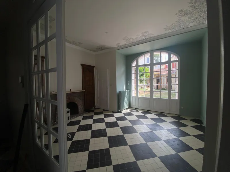 Pièce de réception rénovée en bâti ancien, carrelage damier noir et blanc et porte-fenêtre cintrée